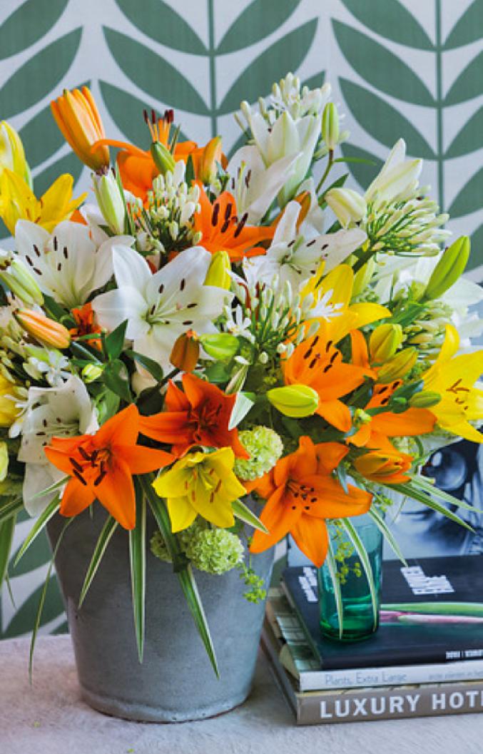 Le bouquet lié classique fait de lis blancs, jaunes et oranges complétés d'agapanthes blanches et d'un feuillage vert liseré de blanc, genre "carex".