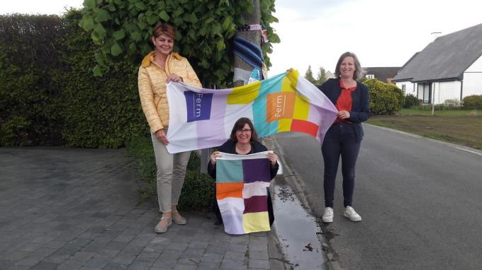 Greetje Lisabeth, Nancy Vanelverdinghe en Els Decock tonen de kleurrijke stroken brei-, haak- en naaiwerk dat in de buurt van de locaties hangt.© TV