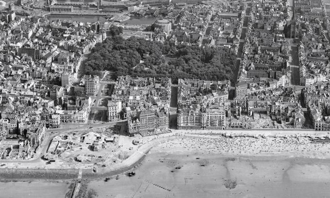 Oostende, 4 augustus 1945: onderaan het totaal verwoeste derde Kursaal en de sterk beschadigde of plat gebombardeerde hotels en dijkvilla’s. Centraal het Leopoldpark voor het doortrekken van de Leopold II-laan en met het geëxplodeerde postgebouw. Het ronde gebouw is het ‘Panorama van de IJzer’ aan het derde handelsdok, dat in 1948 werd gedempt om het stadhuis te bouwen.