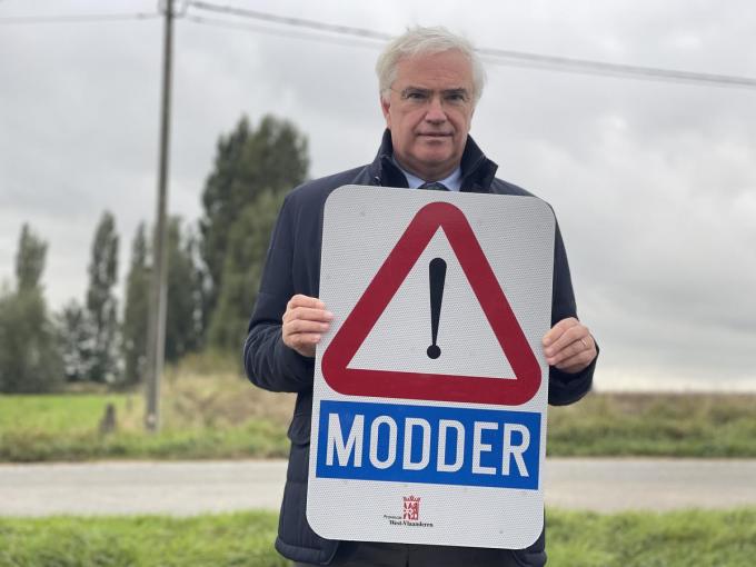 Gouverneur Carl Decaluwé toont een bord dat waarschuwt voor modder op de weg.
