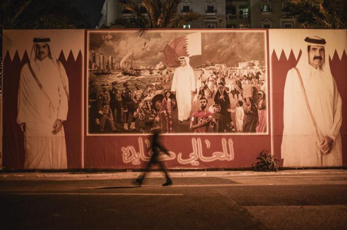 Un travailleur indien passant devant un panneau de propagande chantant les louanges du Qatar et de son émir.