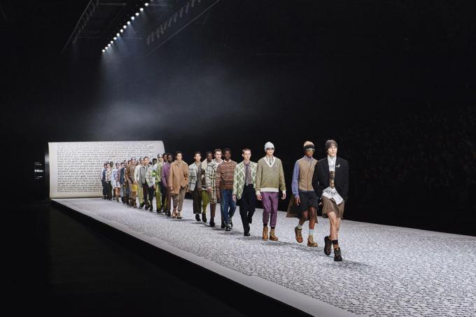 Een beeld uit de finale van de herfstcollectie 2022 van Dior Men: de modellen lopen over een catwalk met tekst uit On the Road van Jack Kerouac.