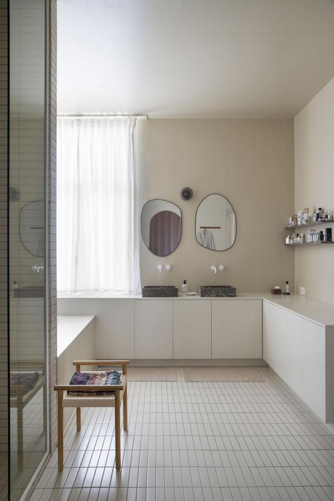 De badkamer kreeg een warme sfeer. Het badkamermeubel dat meerdere muren beslaat, werd gemaakt door De Furniturist. De wasbakken zijn van Rouge Royal en de spiegels van Zara Home.