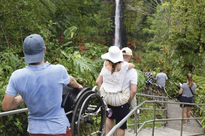 Dans le parc Akaka Falls, à Hawaii, en 2022, Inge est sur le dos de son frère. Son compagnon porte son fauteuil roulant.