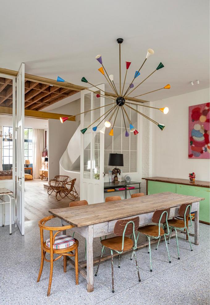Dans la salle à manger, le comptoir vert provient de l’ancien atelier. Le luminaire est un modèle Spoutnik vintage. On aperçoit à l’arrière-plan l’escalier en rondeurs, une des pièces maîtresses de la maison.