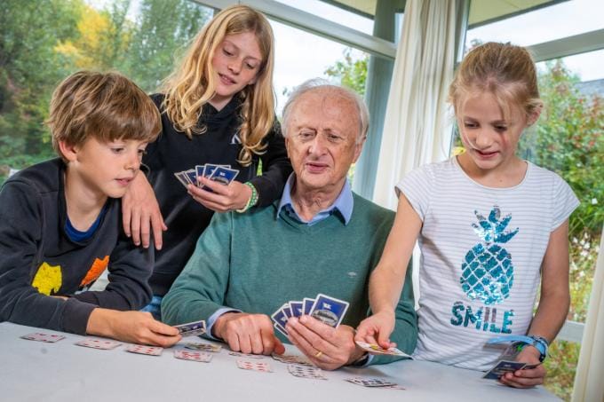 grootvader met drie kleinkinderen spelen een spel kaarten.