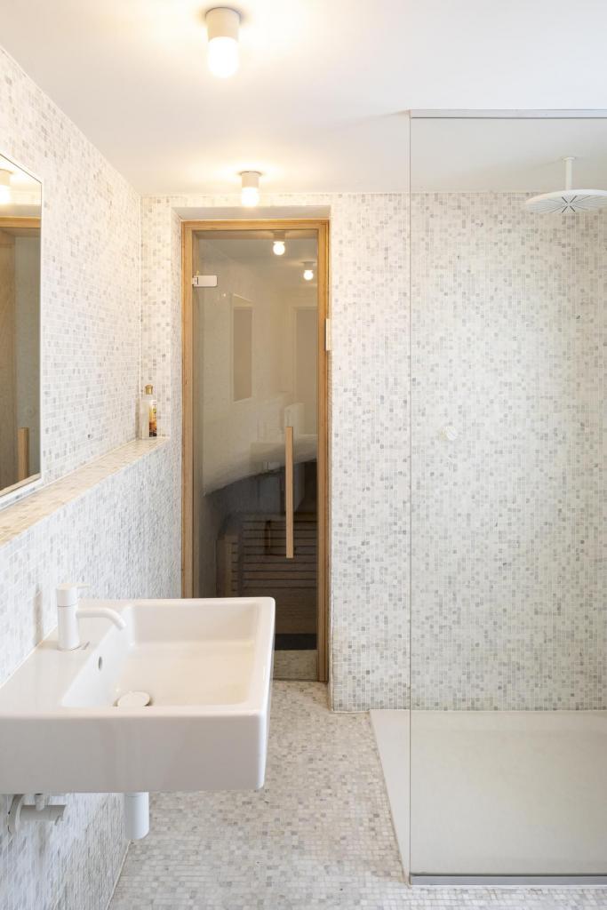 Zowel de badkamervloer als de muren zijn bezet met kleine mozaïektegels. Een minimalistisch geheel met de wittonen en sobere lichte kleur van de Poolse den gebruikt voor het badkamerschrijnwerk. 