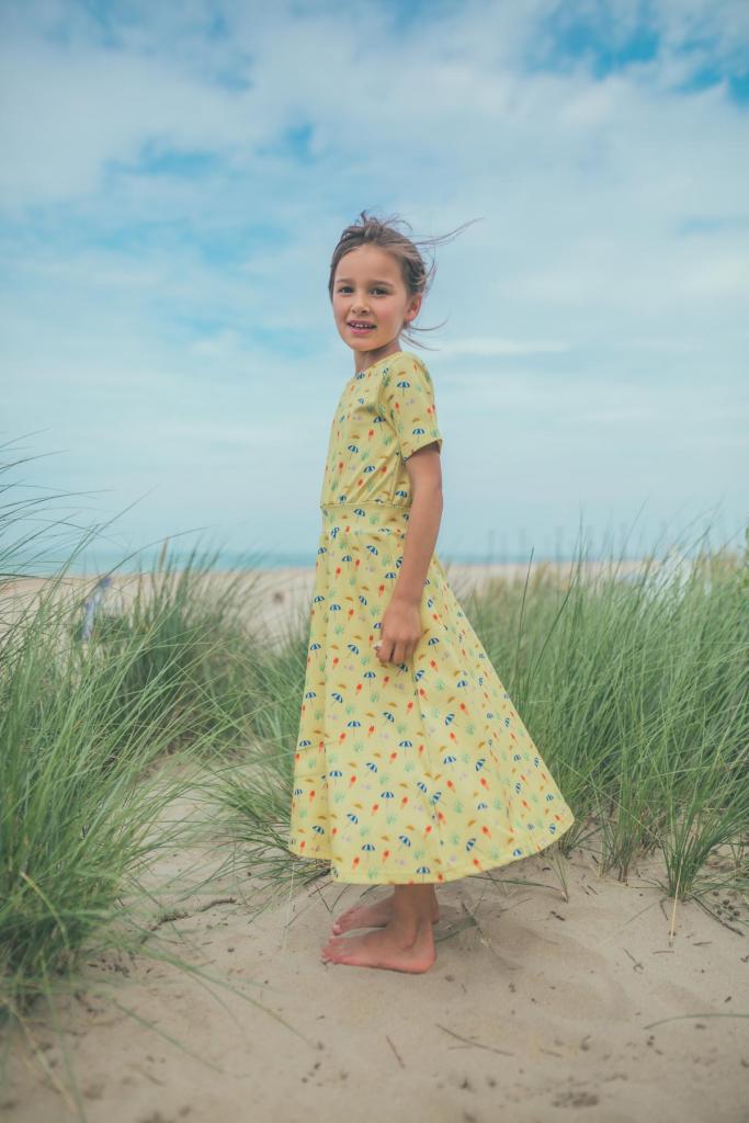 VakantiemoodZachtgele jurk (42,95 euro) met prints van de zon, een parasol en een ijsje: het feest kan niet meer stuk, van Baba Kidswear. 