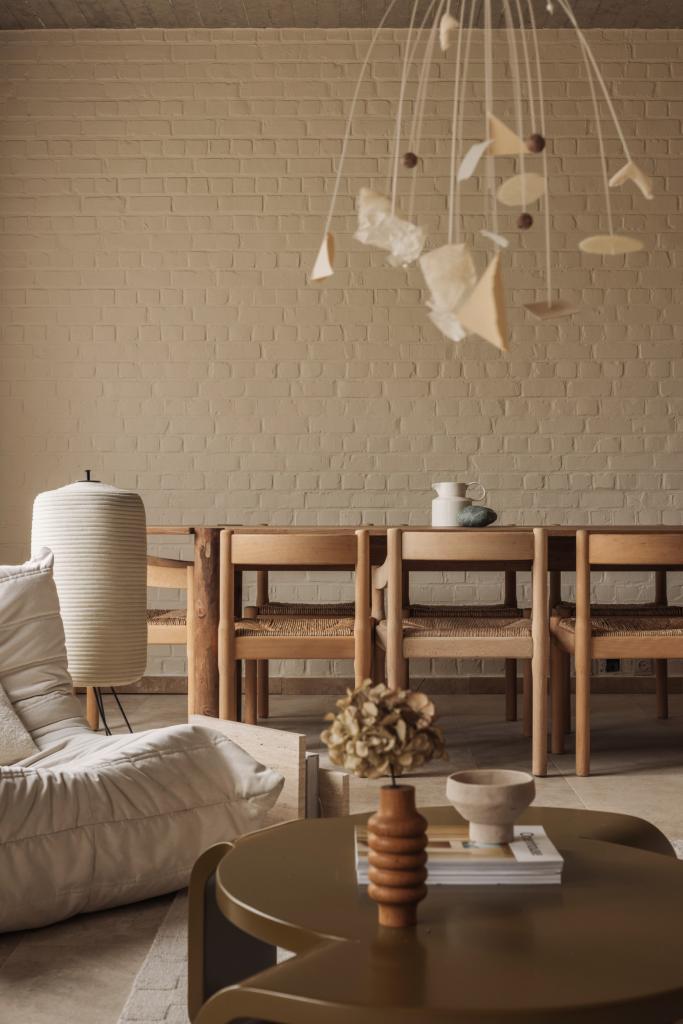 De inrichting van de woning is minimalistisch, doordacht en sereen. Rondom de eettafel staan stoelen van Vico Magistretti Carimate bij Cassina, naast de Togo van Ligne Roset staat een vloerlamp  SHOJI 2 van Davide Groppi. De salontafel is een ontwerp van Wøti, de mobiel Autumn Clouds is van Liene Meneve.