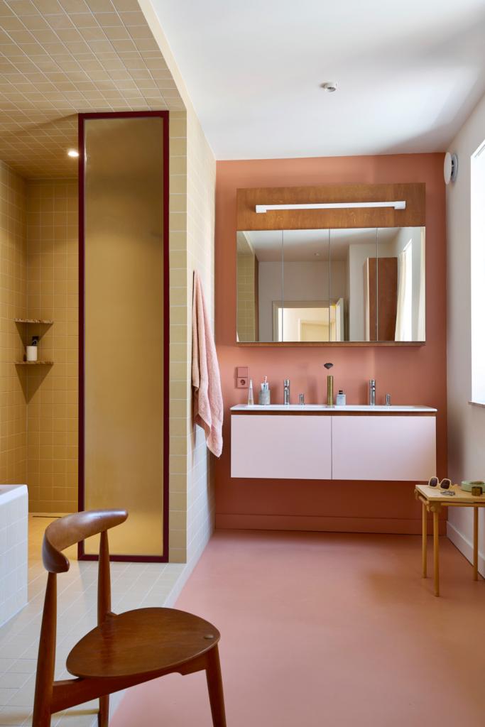Het kleurenpalet van roze, bordeaux en geel uit de keuken keert overal terug; soms subtiel, soms uitgesproken zoals in de badkamer.