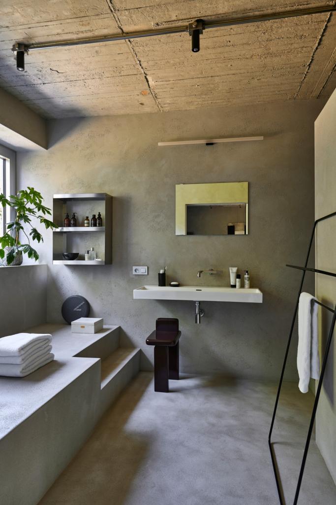 In de badkamer en suite in ruwe beton ciré zorgen de spiegel en de spiegeldeur ertegenover voor een oneindig perspectief.