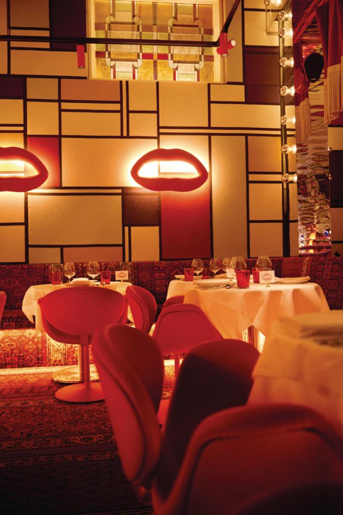 Restaurant Bisous in Amsterdam. ‘De enige originele elementen in de volledig witte ruimte zijn de glas-in-loodramen. Ze deden me meteen denken aan Mondriaan, al hebben we de kleuren aangepast om die link subtiel te houden. De rode betonnen lippen tegen de muren zijn een experiment van een van onze ambachtsmannen. Ook de Nederlandse Artifort-stoelen verwijzen naar lippen.’