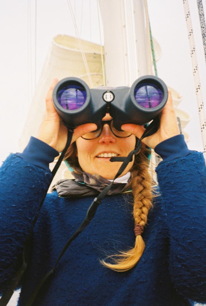 Vrouw met verrekijker op zeilboot