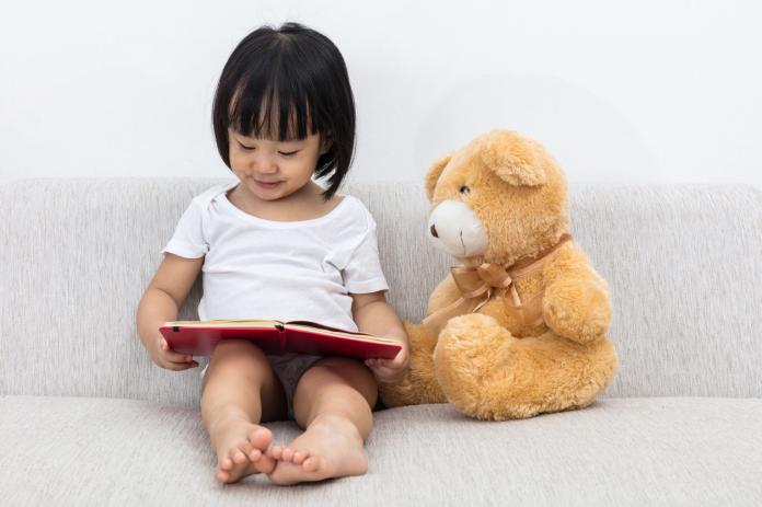 Asian Chinese little girl reading book with teddy bear