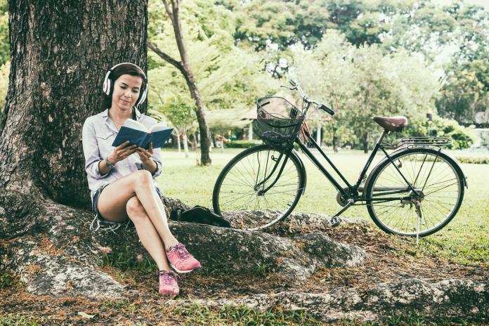 Woman reading a book while listening music in a park