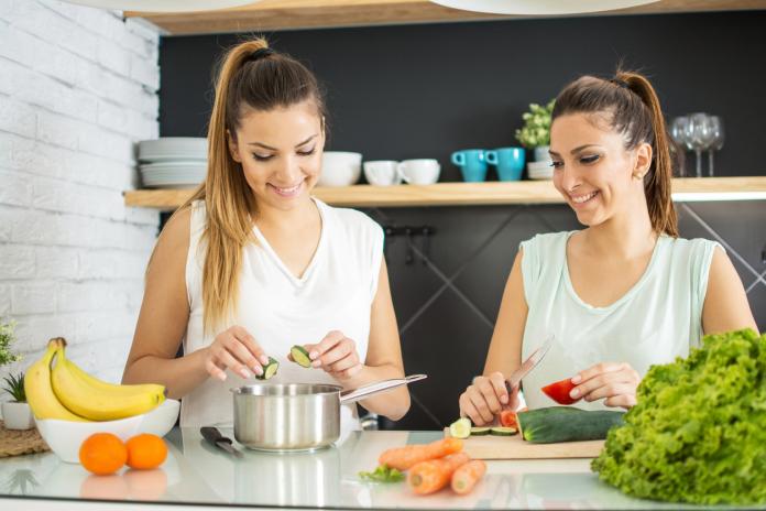 Young twin sisters preparing organic vegetables salad in the kitchen.