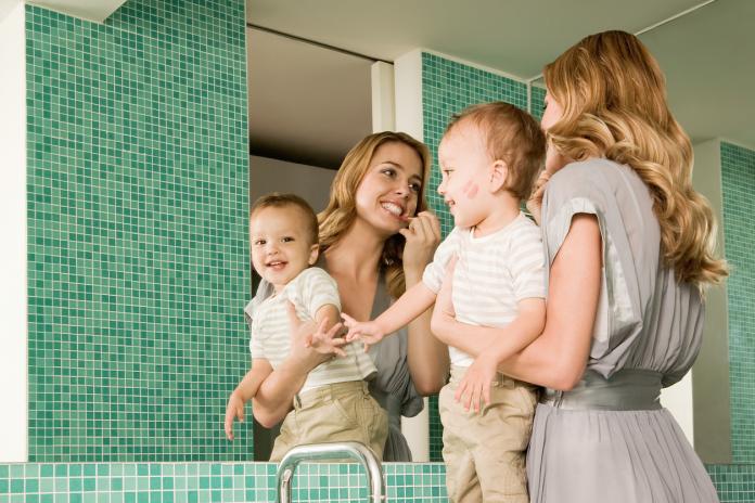 Woman holding baby and putting on lipstick