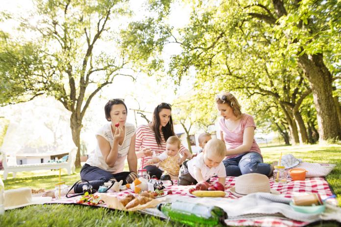 Three mothers outdoors in green nature with their children having picnic.