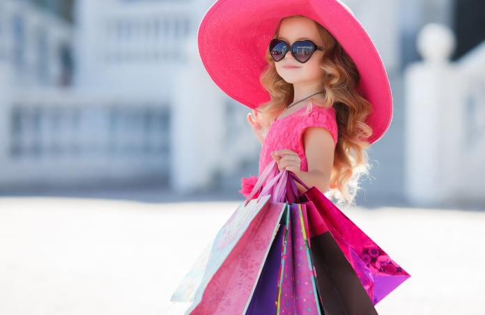 Cute little girl in fashion hat with shopping bags next to a supermarket
