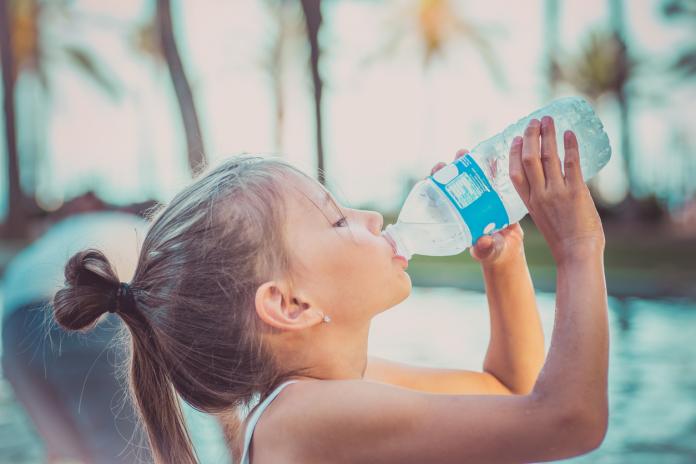 A child is drinking clean water from a bottle. Hot summer day.