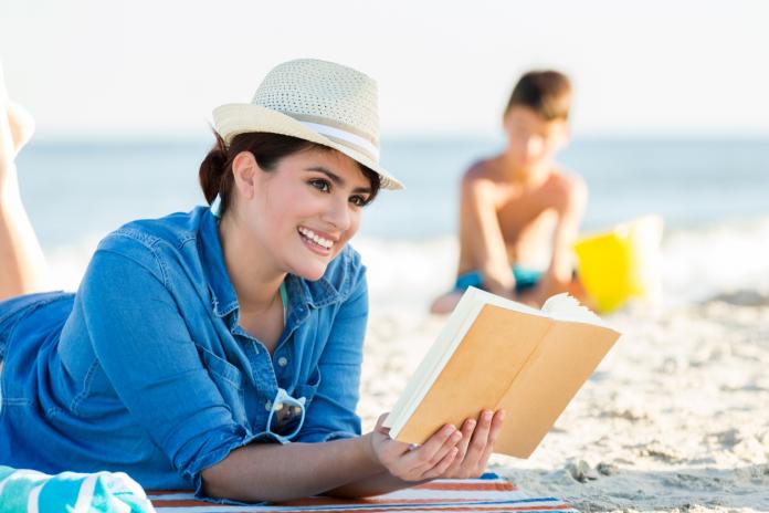 Relaxed woman reads book on sandy beach