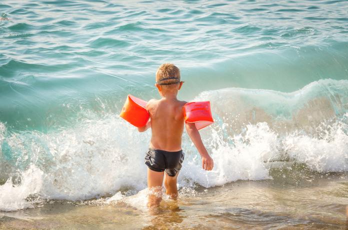 child runs in the sea with protective inflatable sleeves