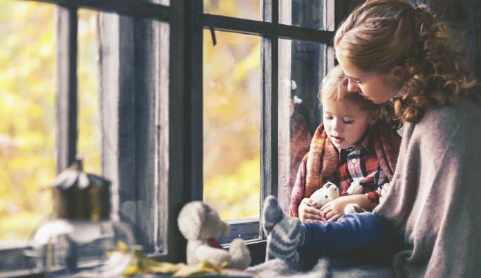 family mother and child look out window on rainy autumn