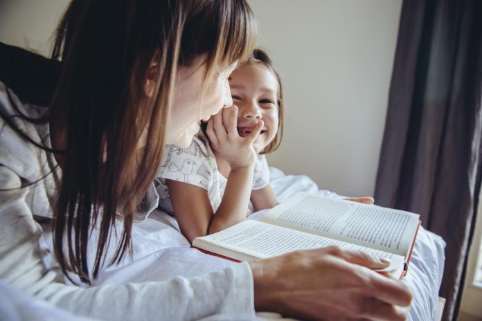 Mother and daughter reading book in bed