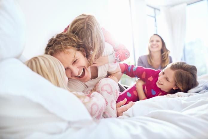 Playful father and daughters tickling on bed