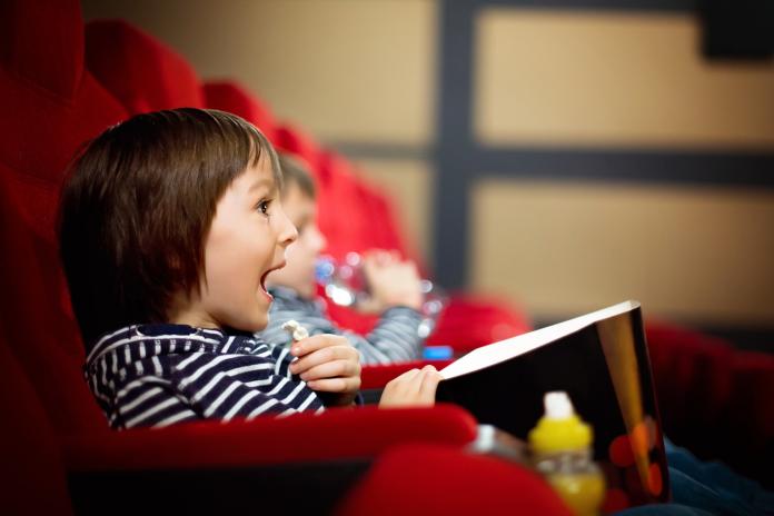 Two preschool children, twin brothers, watching movie in the cinema, eating popcorn