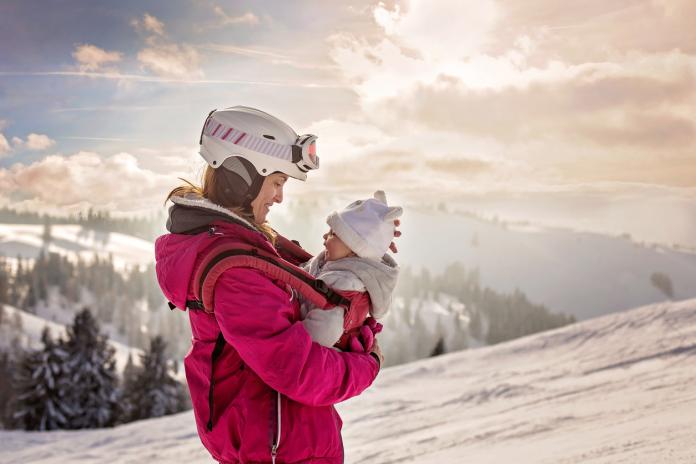 Young mother, carrying her baby boy in sling, climbing on peak wintertime, Austrian Apls