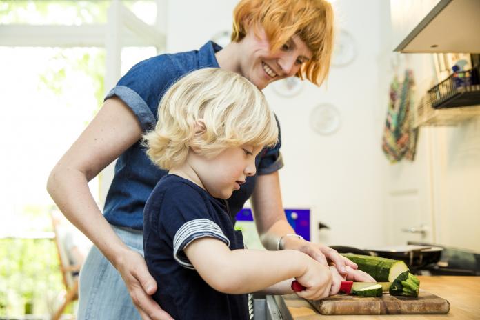 Littel boy chopping vegetables in the kitchen while his mother watching him samen koken met je kind