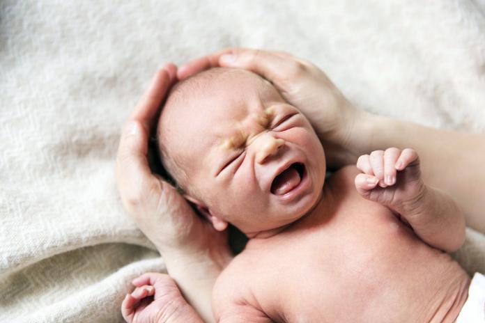 High angle view of hands cupping crying baby boys head baby laten huilen