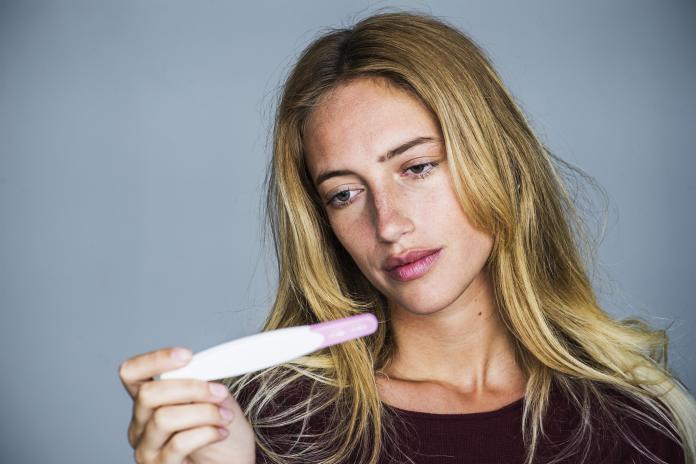 Young woman looking at pregnancy test with disappointed expression negatieve zwangerschapstest