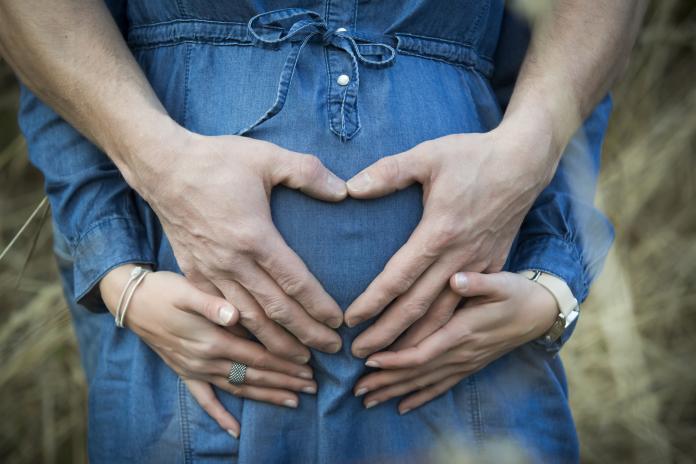 Hand of man forming heart on the belly of his pregnant girlfriend
