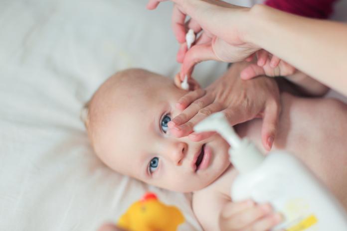 a Young mother cleans her baby boy's ears.