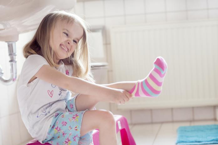 Child (4-5) pulling socks on with determined facial expression zweetvoeten kind