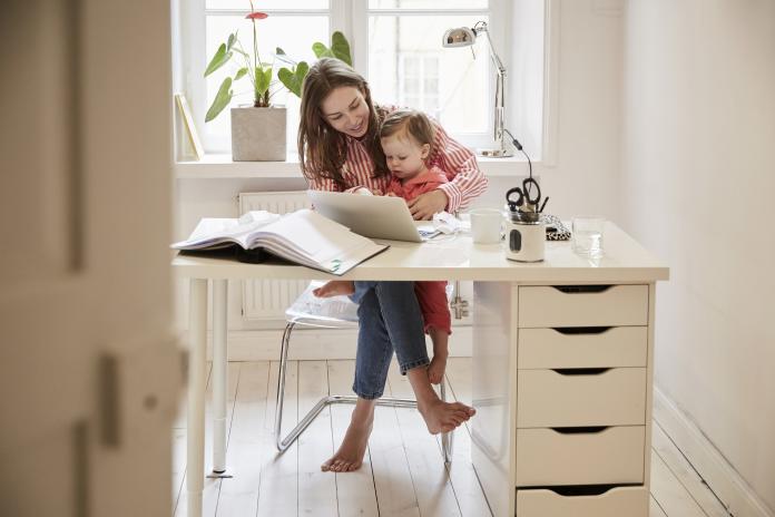 Female accountant sitting with daughter while working on laptop at home