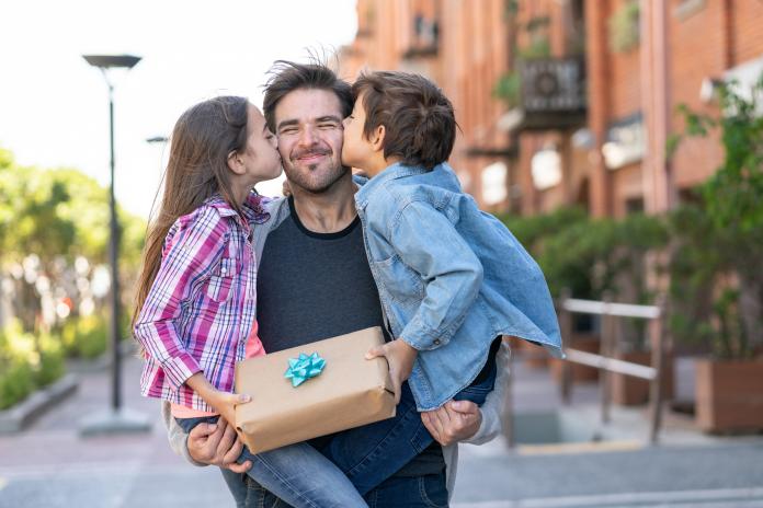 Loving son and daughter kissing daddy on the cheek while he carries them both with a present for father's day duurzame cadeautps Vaderdag