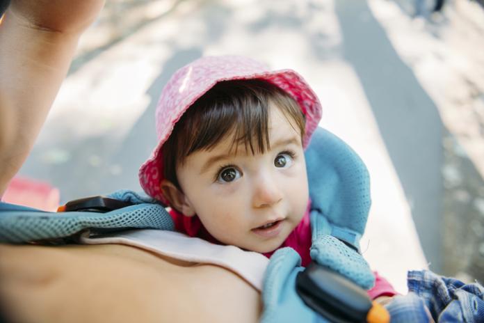 Cute baby girl travelling with mum in a baby carrier