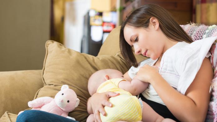 Young mom breastfeeding infant daughter at home