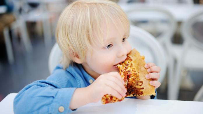 Cute blonde boy eating slice of pizza at fast food restaurant