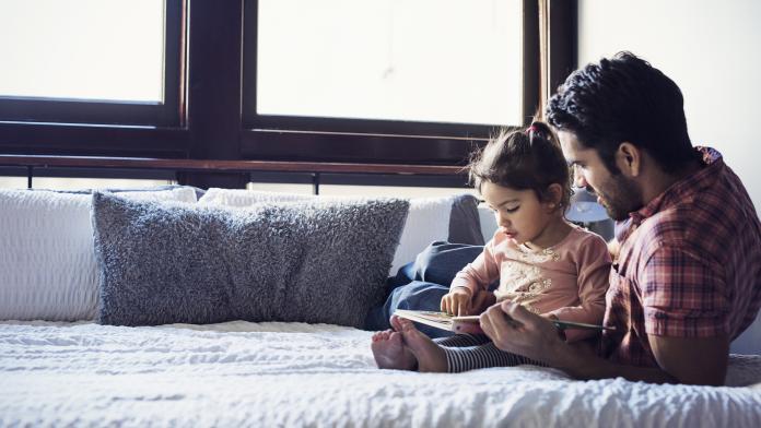 Father and daughter reading book, lying on bed