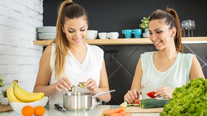 Young twin sisters preparing organic vegetables salad in the kitchen.