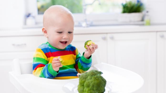 Little boy eating broccoli in white kitchen