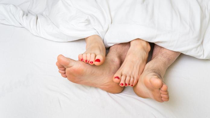 Feet of a couple in bed under the blanket