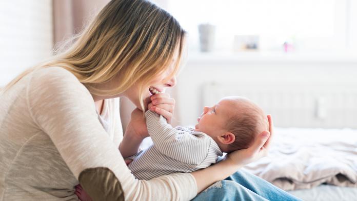 Mother with her newborn baby son sitting on bed