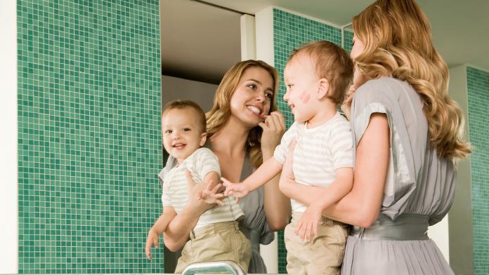 Woman holding baby and putting on lipstick