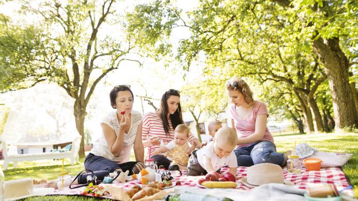 Three mothers outdoors in green nature with their children having picnic.