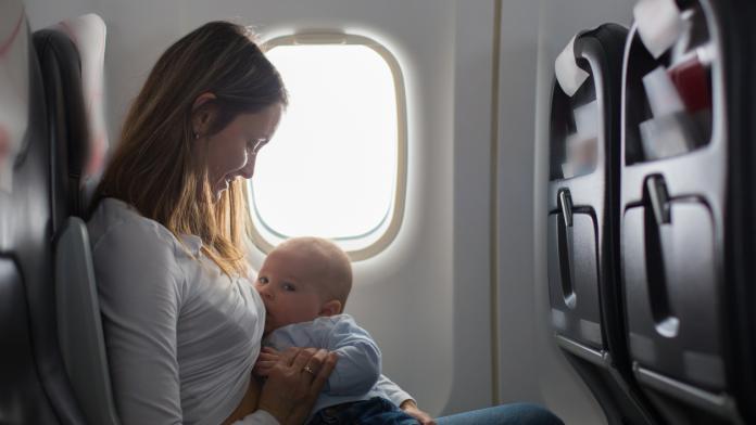 Young mom, playing and breastfeeding her toddler boy on board of aircraft